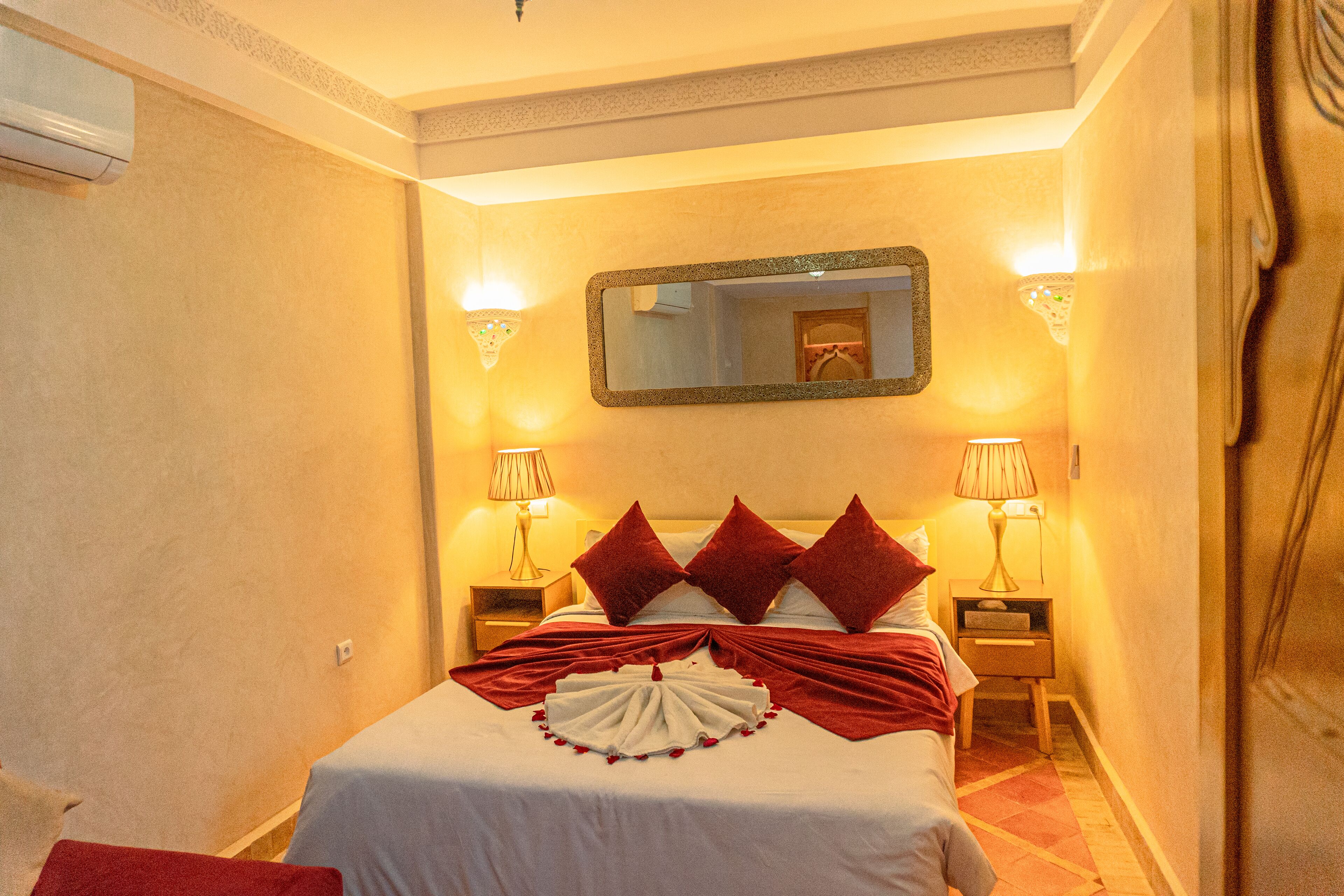 Habitación de hotel con una cama, dos mesitas de noche, un espejo y lámparas fijadas a la pared.