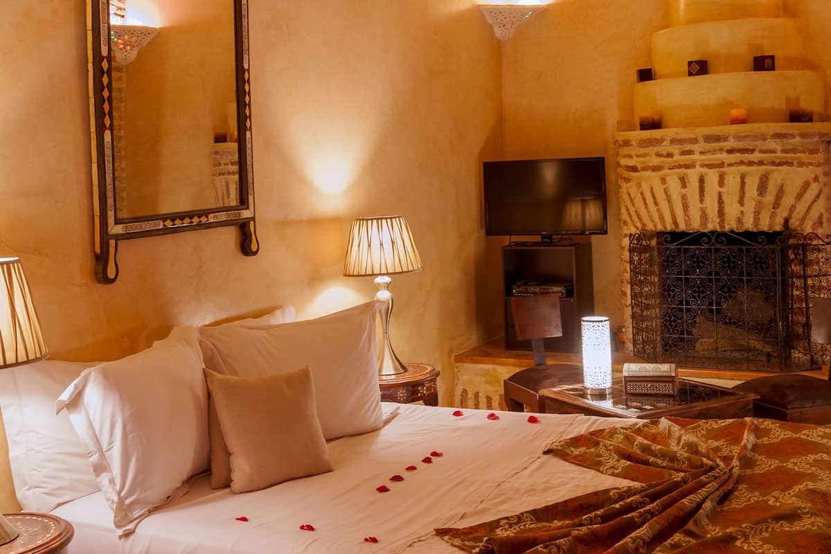 A bedroom with a bed, a large mirror, a television, a fireplace, and a decorative hanging light fixture.