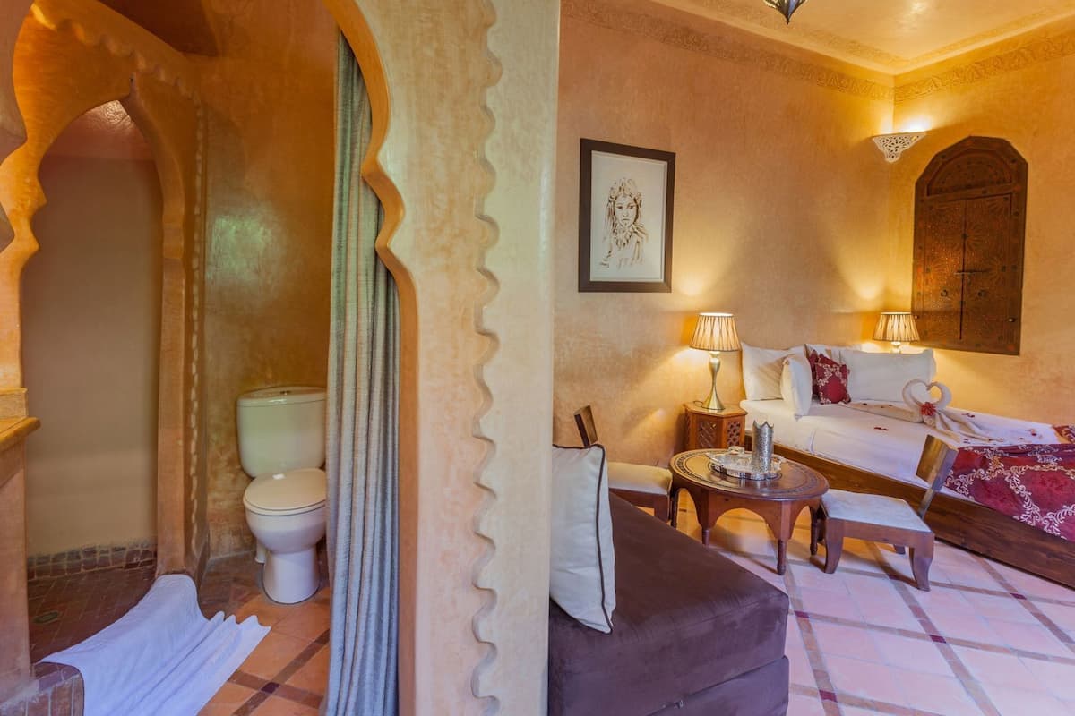 A room with a traditional design, including a bed, a sofa, a small table, and a toilet.