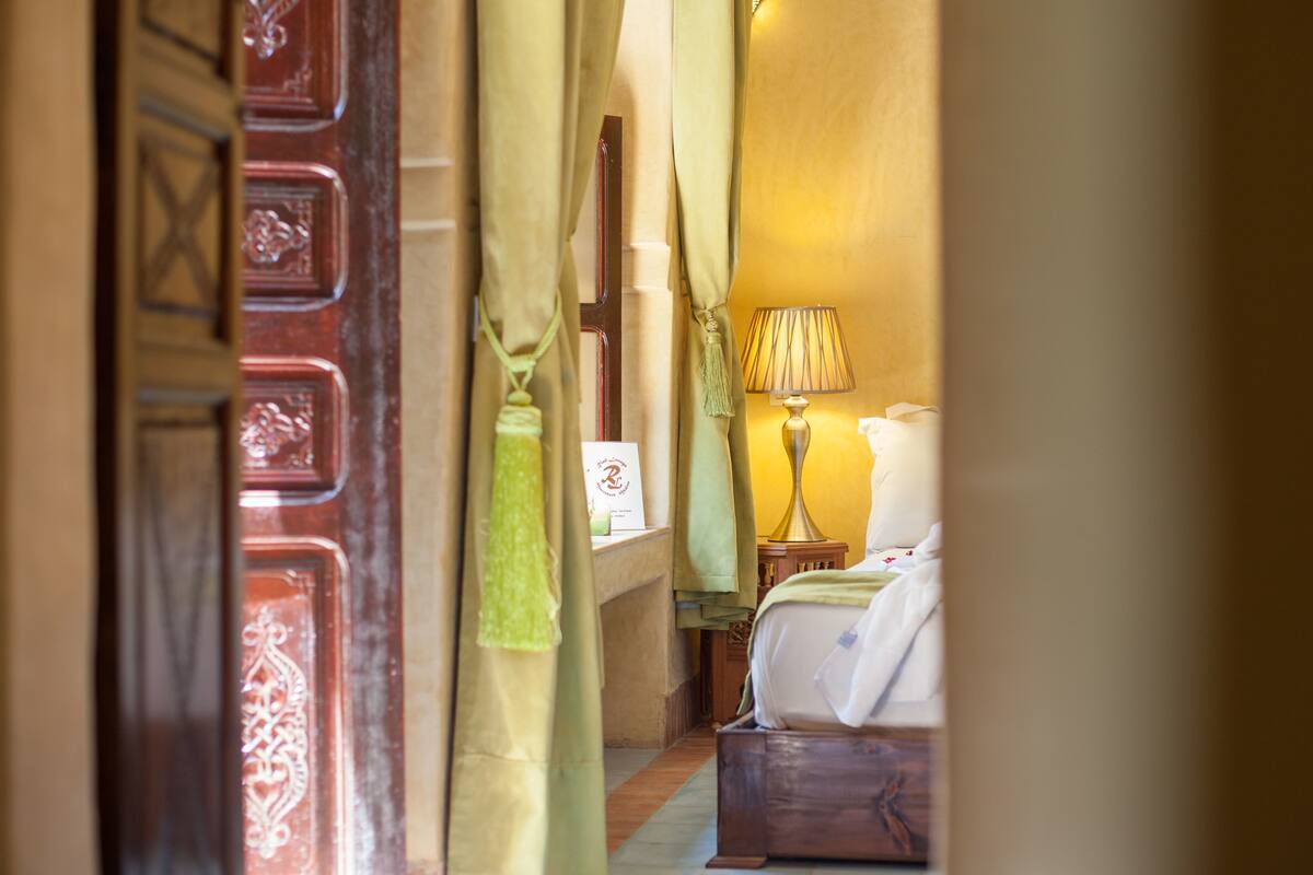 A hotel room with a bed, a nightstand, a lamp, and a door with decorative panels.