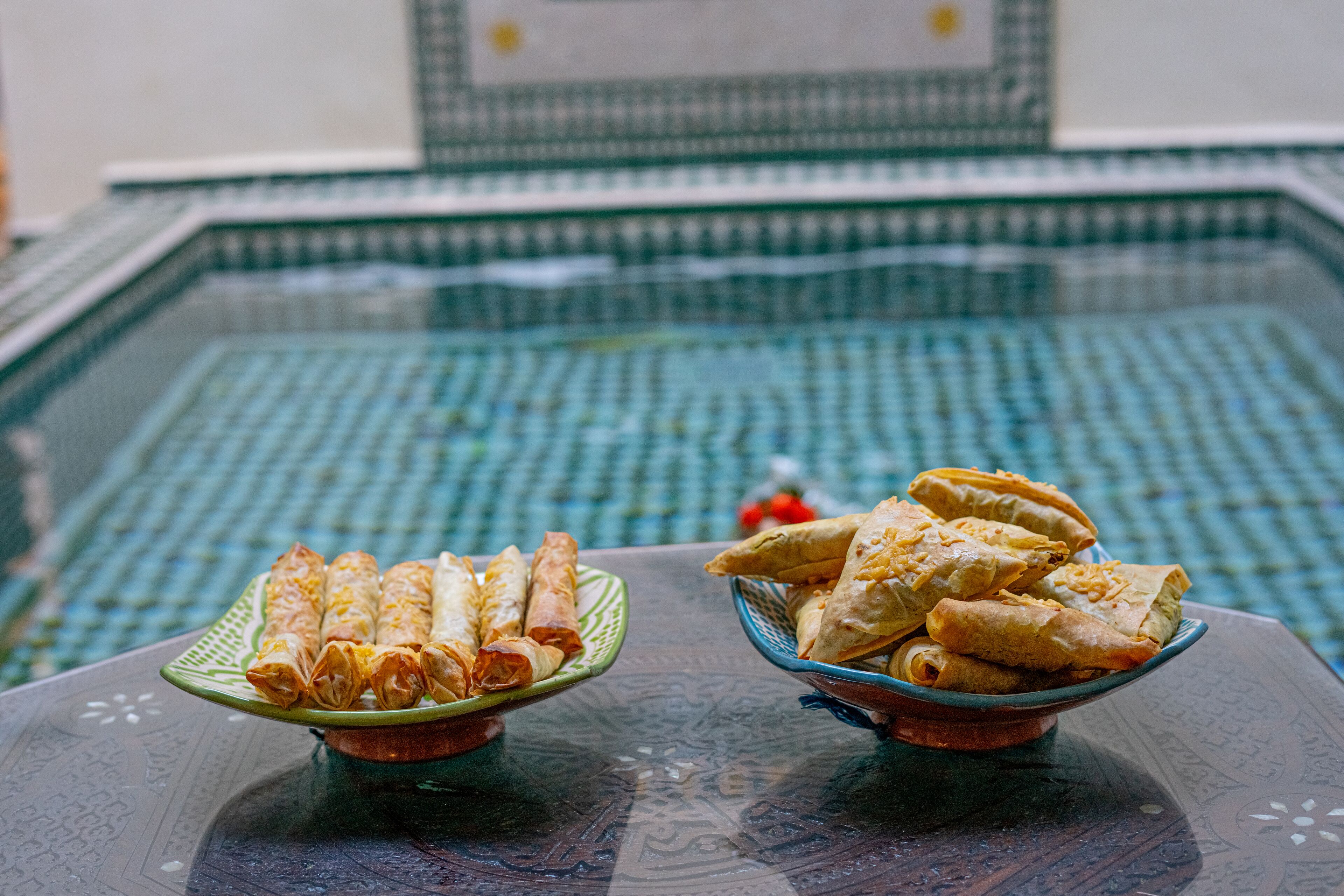 Two bowls of fried spring rolls on a table with a tiled floor.