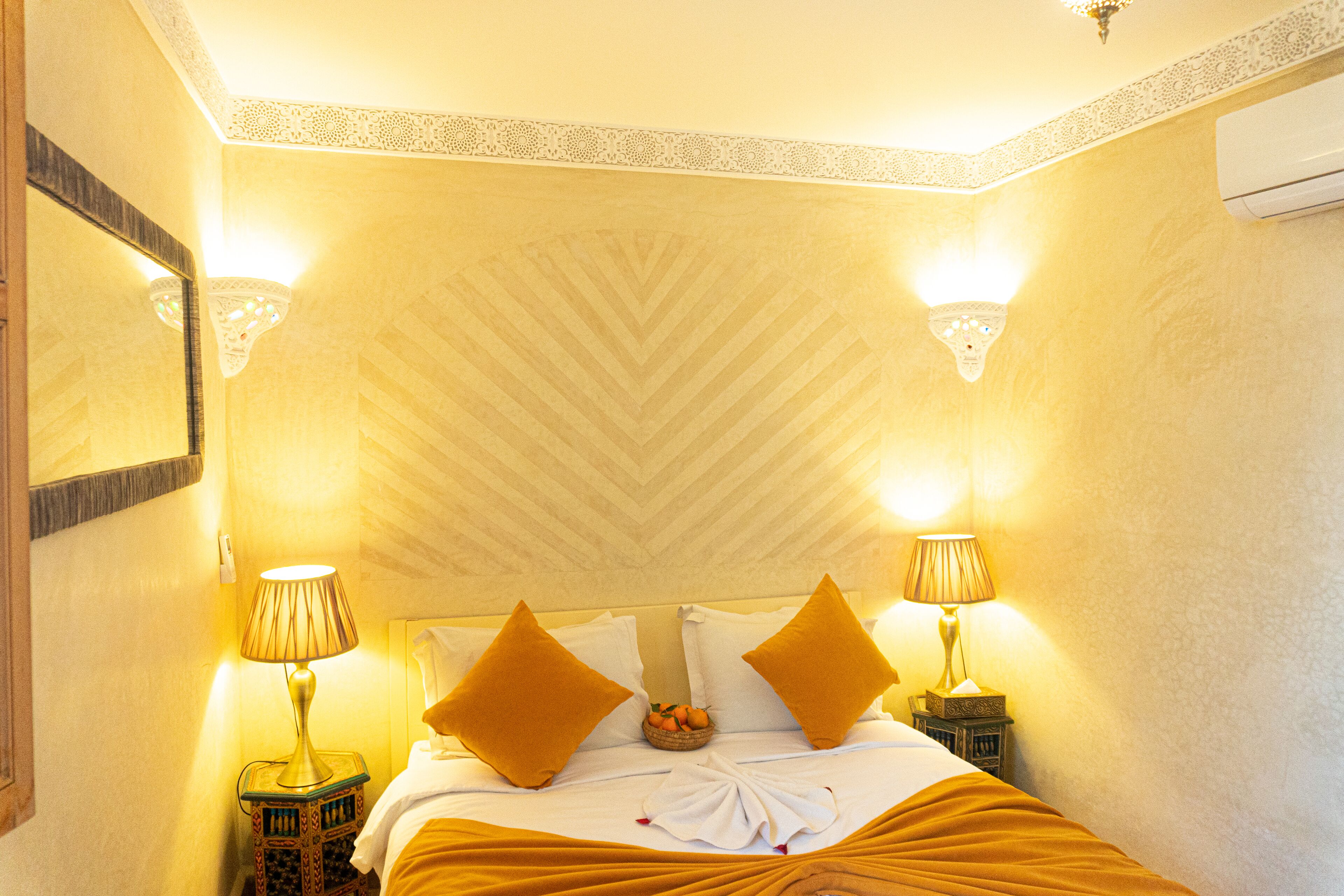 A hotel room with a bed, two lamps, a mirror, and a decorative wall pattern.