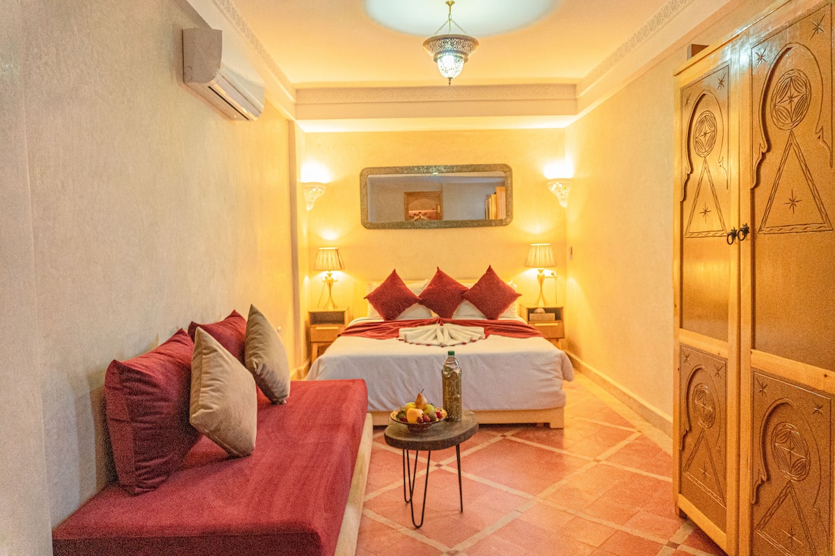 A hotel room with a bed, a sofa, a small table with fruit, and a wardrobe.