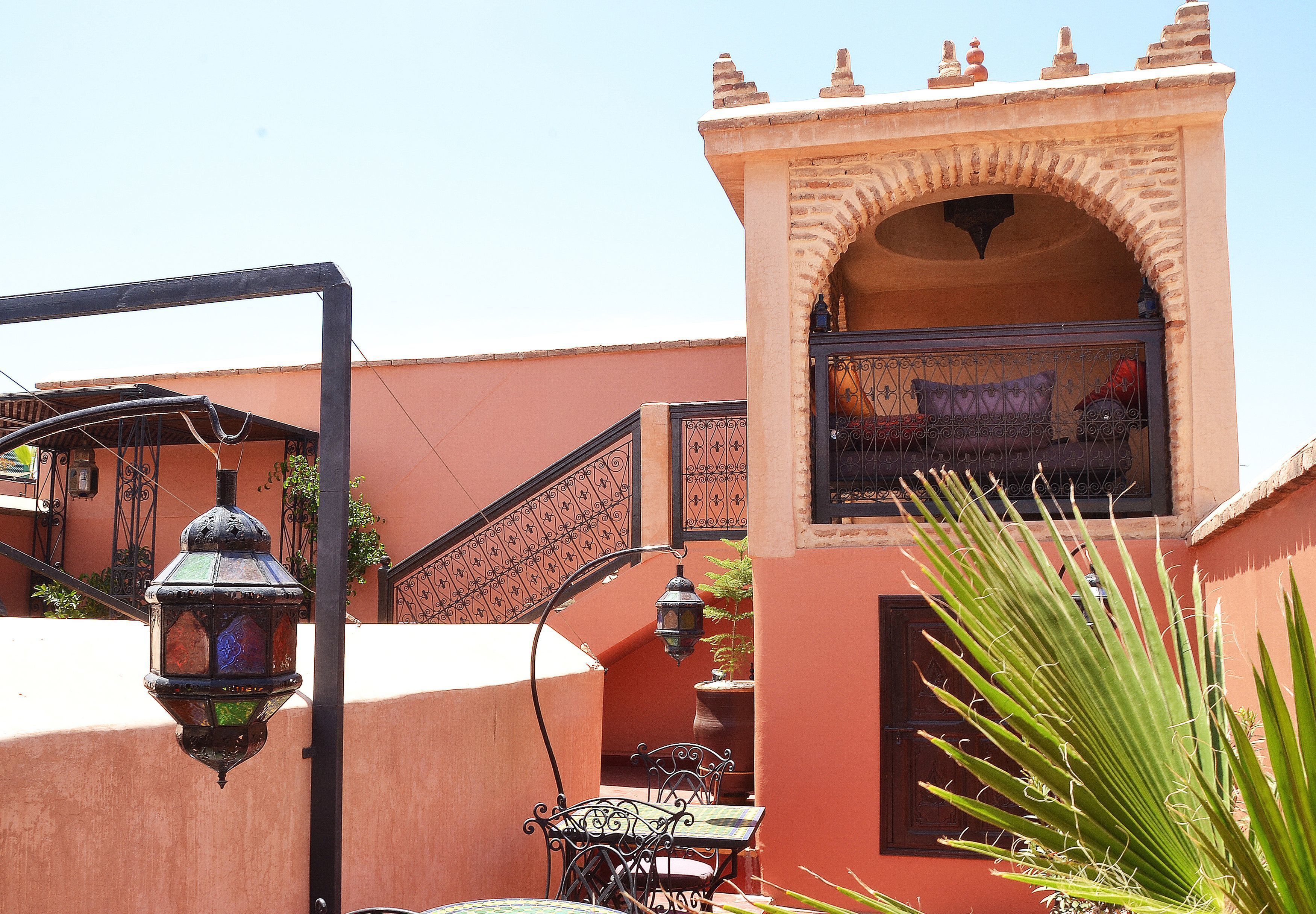 A traditional Moroccan courtyard with a wrought iron gate, a hanging lantern, and a palm plant.