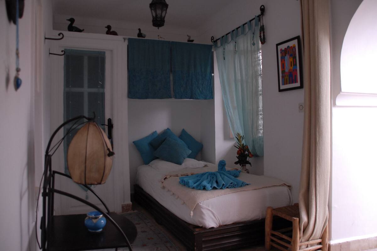A bedroom with a bed, a nightstand, a lamp, and a window with curtains.
