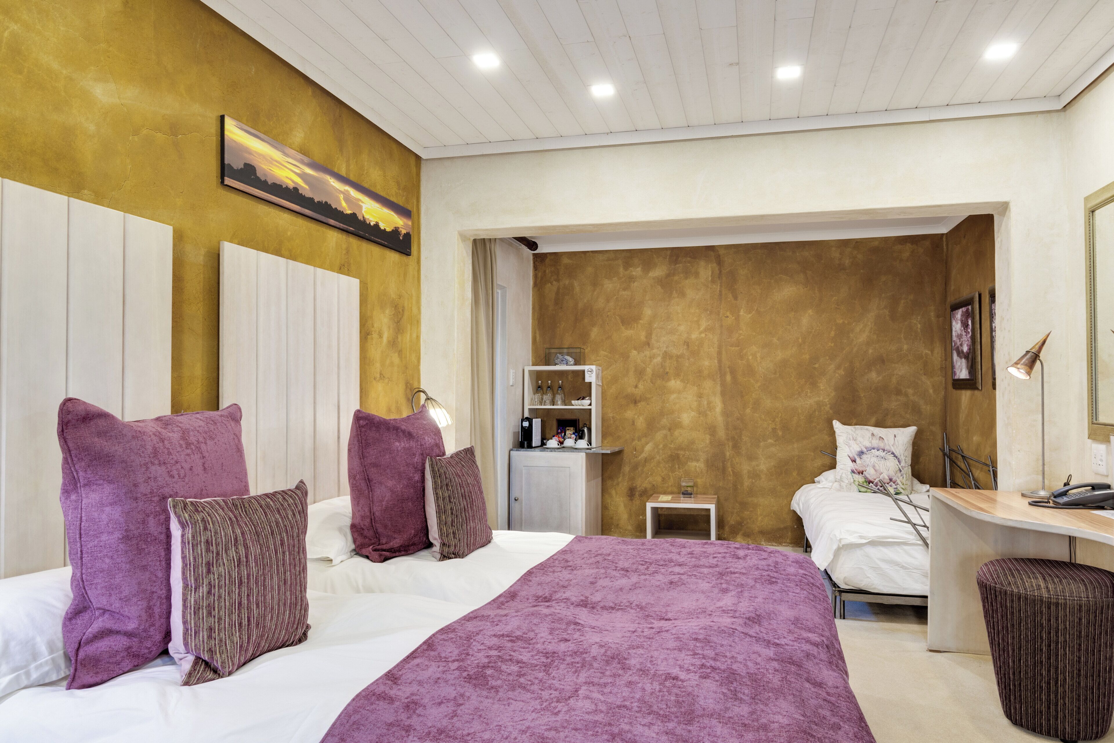 A bedroom with a bed, bedside table, lamp, and a small desk area.