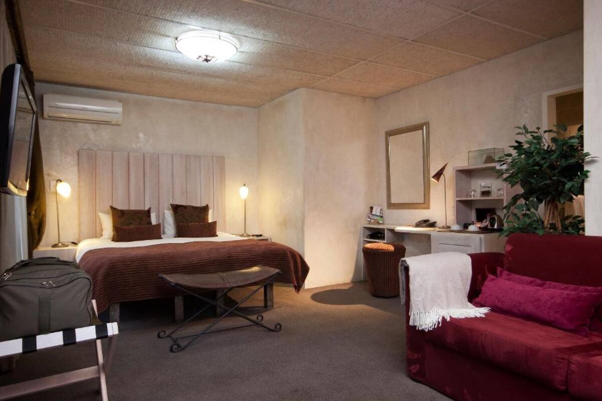 Habitación de hotel con cama, mesita de noche, lámpara, escritorio, silla y sofá rojo.