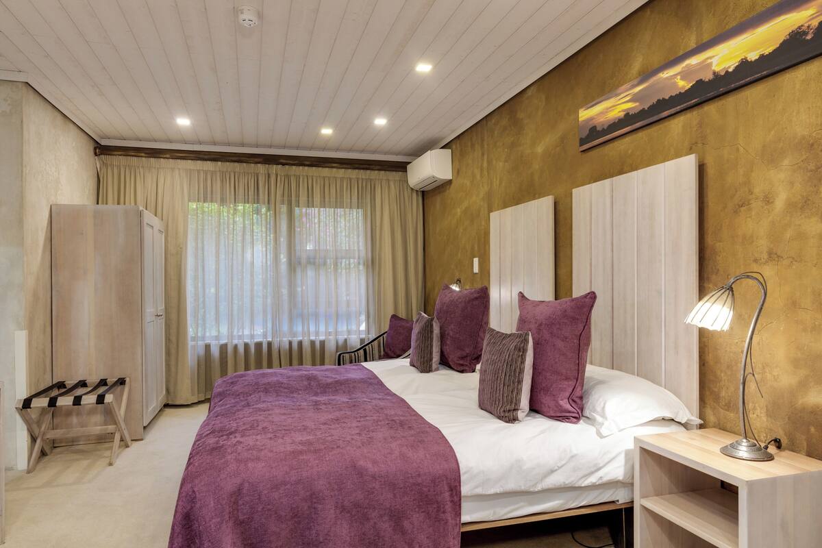 Un dormitorio con cama, mesitas de noche, armario, ventana con cortinas y unidad de aire acondicionado.