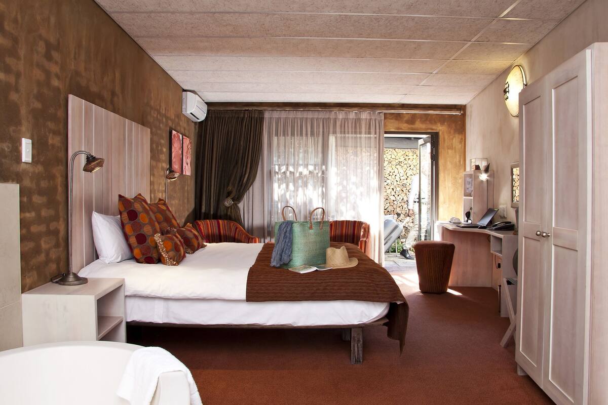 Habitación de hotel con cama, mesitas de noche, escritorio con ordenador, silla y ventana con cortinas.