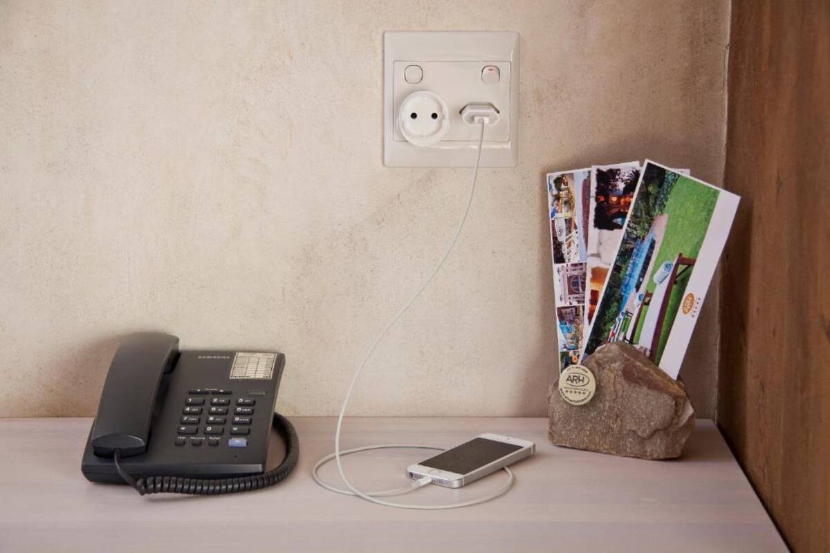 Un escritorio con un teléfono fijo, un teléfono inteligente conectado a un enchufe y una roca con postales.