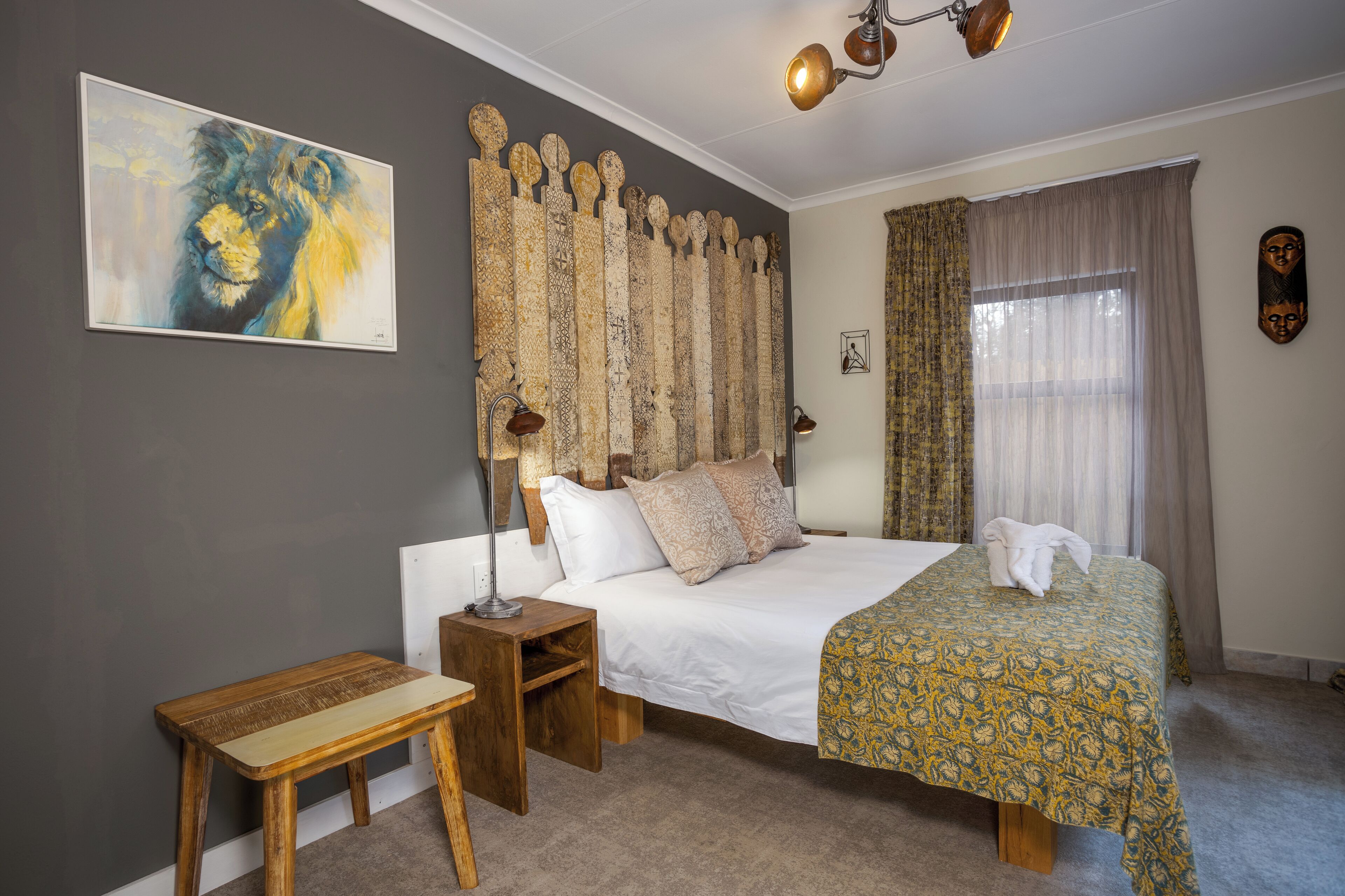 Una camera da letto con un letto grande, un comodino in legno, una panca, un quadro, una testiera decorativa e una finestra con tende.