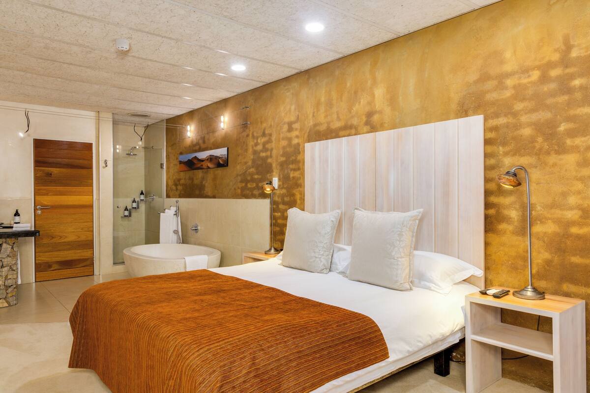 Una habitación de hotel moderna con una cama grande, baño con ducha y un panel de madera decorativo.