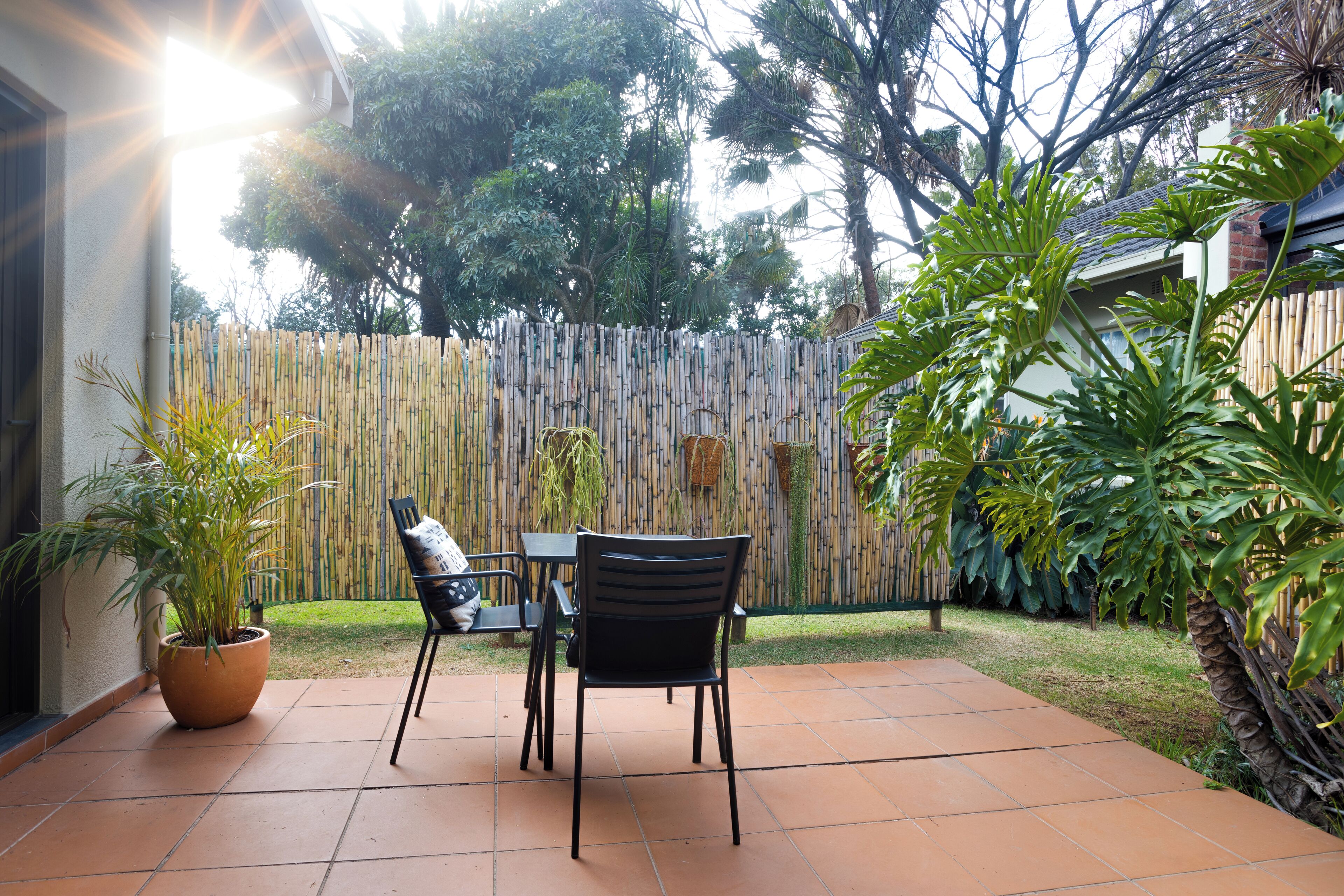 An outdoor patio with a table and chairs, surrounded by a bamboo fence and tropical plants.