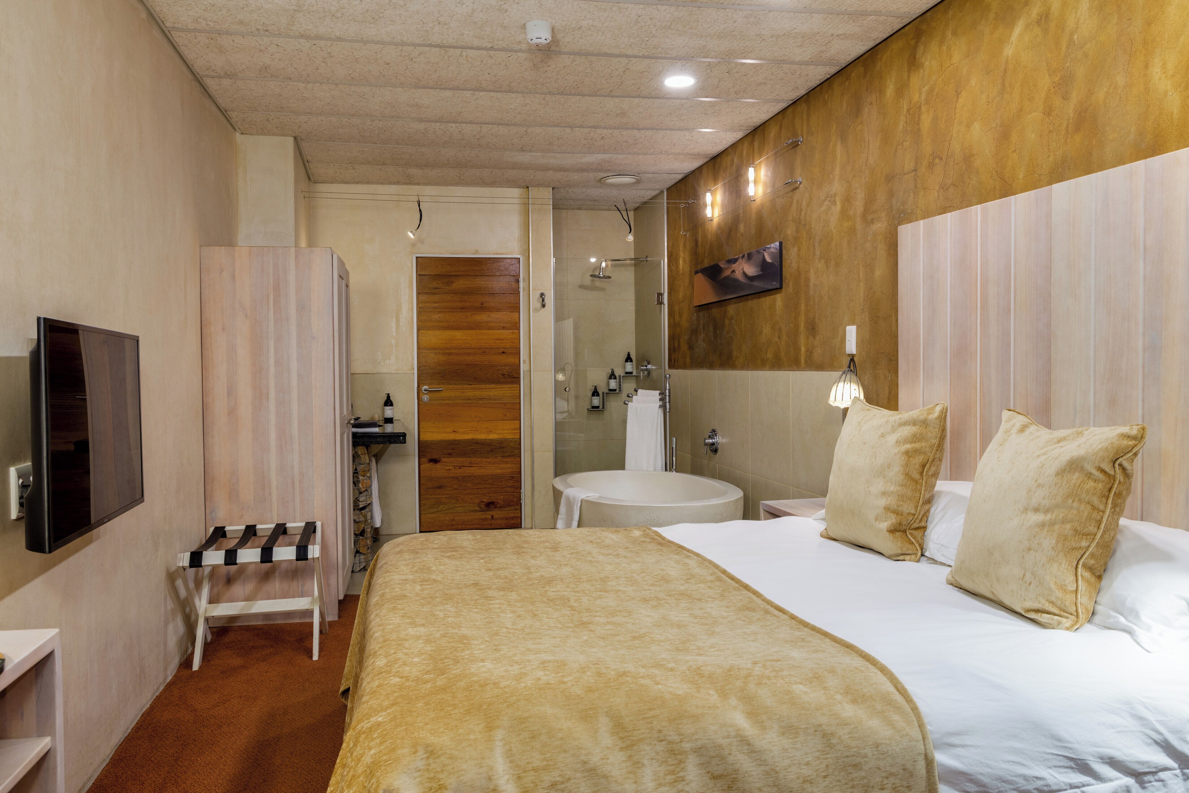 A hotel room with a bed, a TV, a bathroom, and a small seating area.