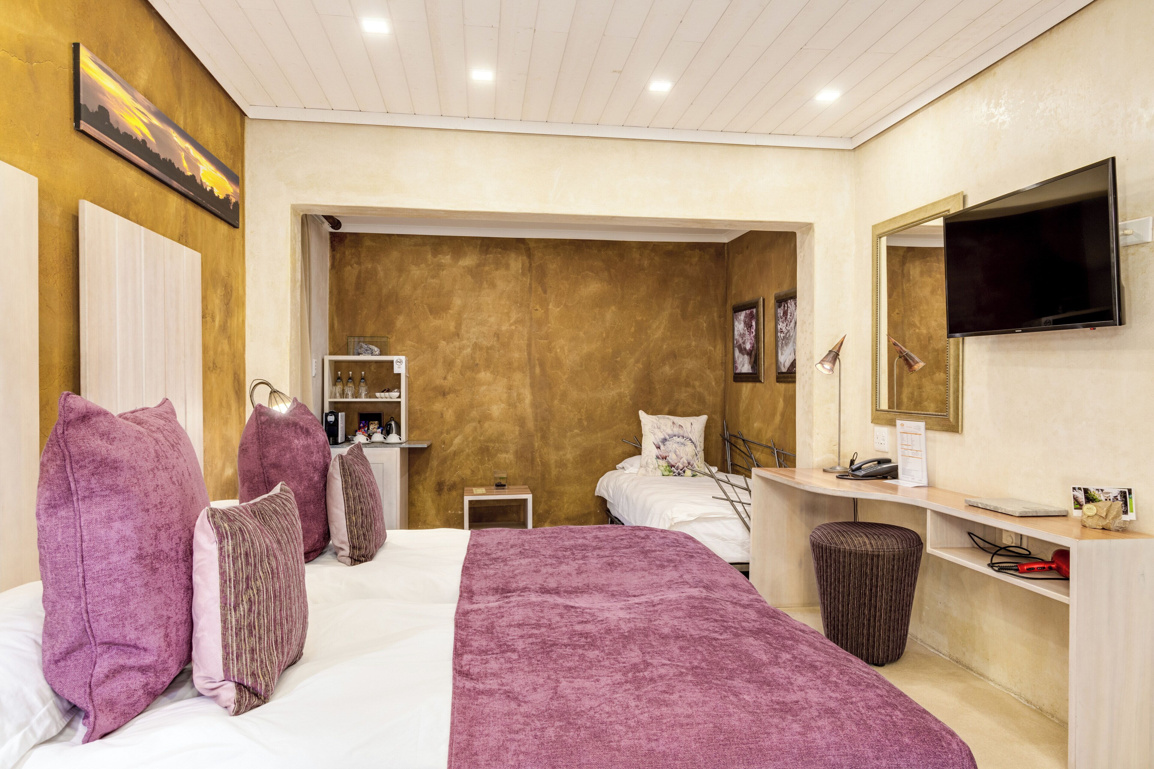 Ein Hotelzimmer mit Bett, Schreibtisch, Fernseher und einem durchgegangenen Tür erkennbaren Badezimmer.