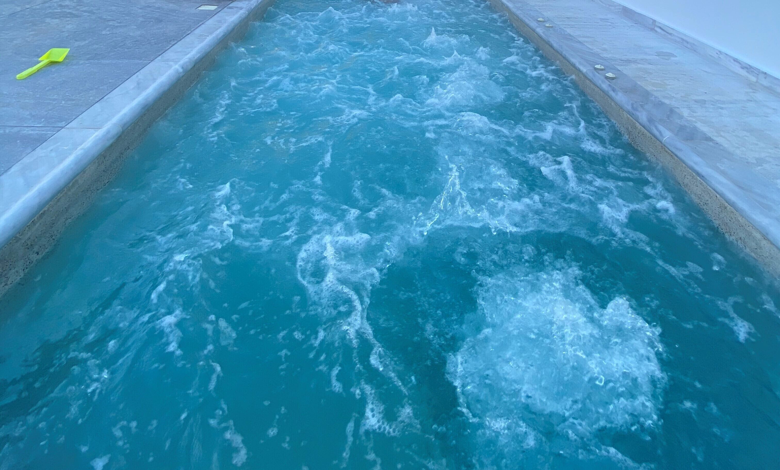 A pool with clear blue water and a yellow shovel on the edge.