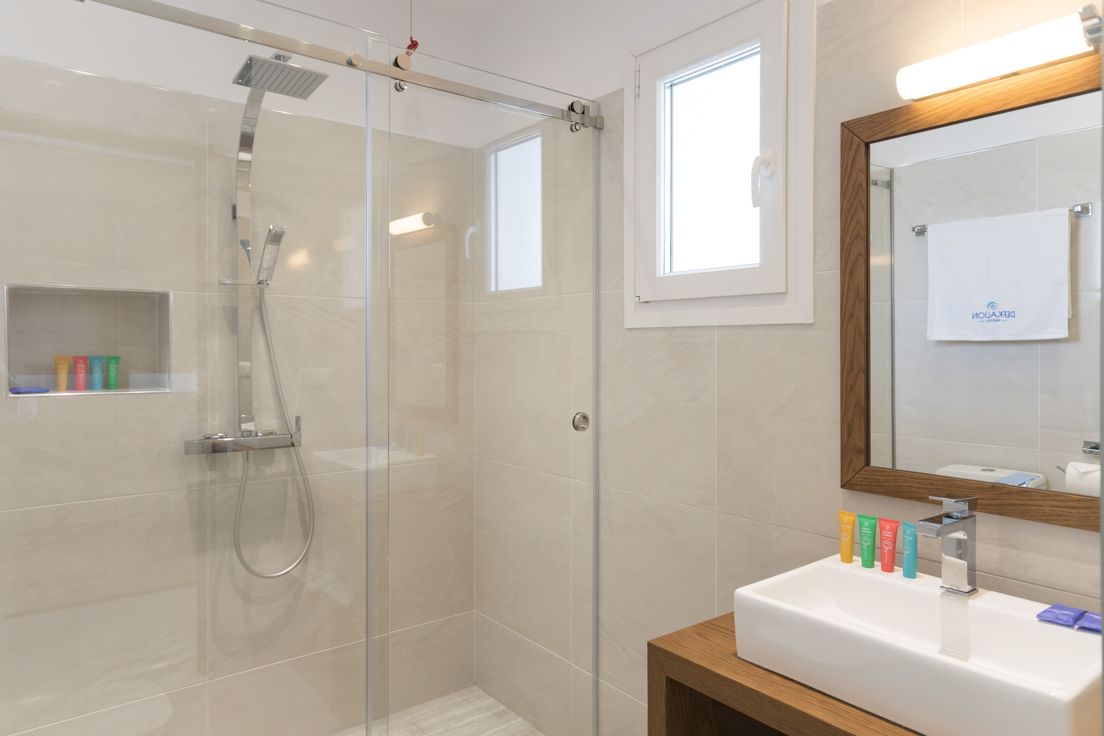 Un baño moderno con ducha de vidrio, un lavamanos blanco y dispensadores de jabón de colores, y un mueble de tocador de madera.