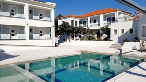 A modern hotel with a swimming pool, white exterior, and red-tiled roof.