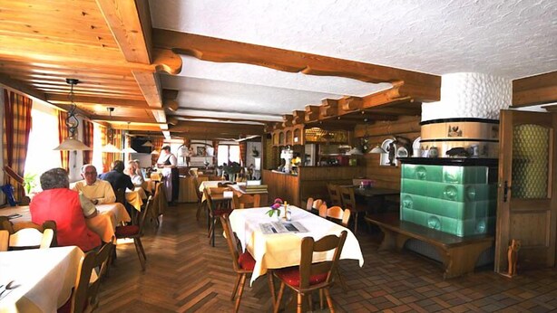 Een restaurant met houten inrichting, tafels met witte tafelkleden en een bar.