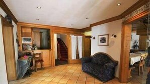 Een ruime woonkamer met betegelde vloer, een bank, een eettafel en een trap naar een andere kamer.