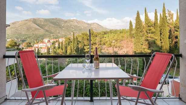 A balcony with a table, two red chairs, a bottle of wine, and a glass. - Apartments Karacic (Konavle)