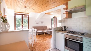 A modern kitchen with a wooden ceiling, a dining area with a sofa and chairs, and a view of the outdoors. - Apartments Karacic (Konavle)