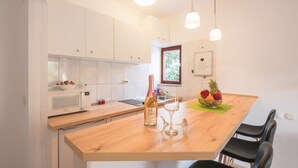 A modern kitchen with white cabinets, a wooden countertop, a microwave, a wine bottle, two glasses, and a fruit bowl. - Apartments Karacic (Konavle)