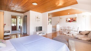 A modern hotel room with a wooden ceiling, a large bed, a sofa, a TV, and a dining area with chairs and a table. - Apartments Karacic (Konavle)