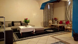 A living room with a sofa, a table with a vase of flowers, a patterned rug, and a blue accent wall. - Ksar Tinsouline (Zagora)