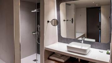 A modern bathroom with a glass-enclosed shower, a white sink, and a large mirror.