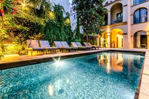 A swimming pool with lounge chairs, surrounded by lush greenery and a building with arched windows. - Hotel Nord 1901 (Girona)