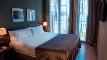 A hotel room with a large bed, two bedside lamps, a nightstand, and a view of the outdoors through sheer curtains.