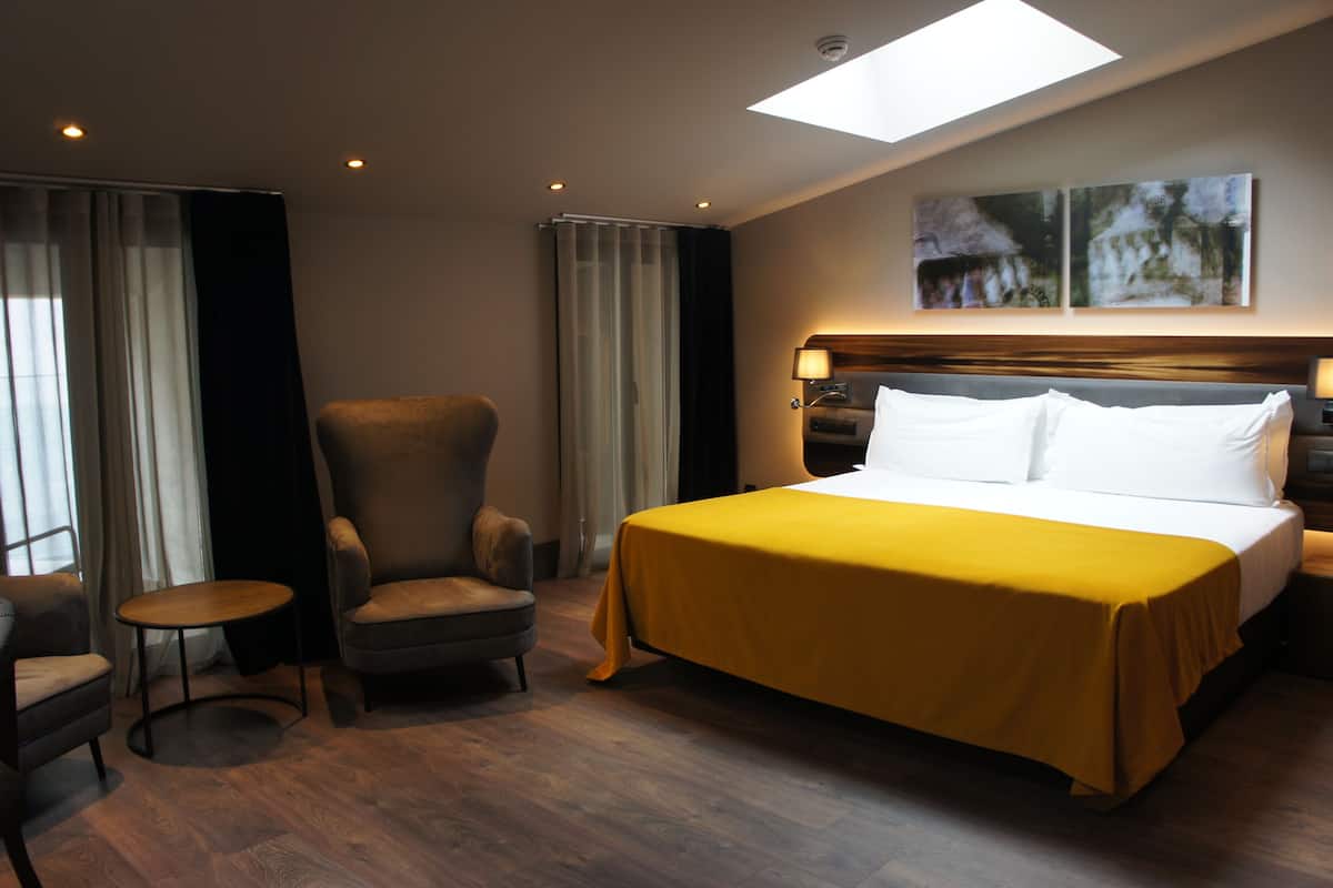 Una habitación de hotel con una cama grande, una silla, una mesita y un tragaluz.