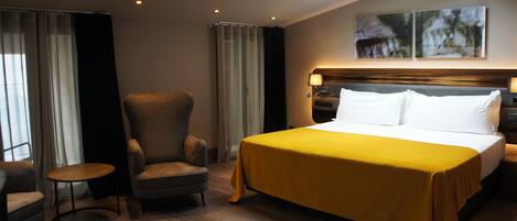 A hotel room with a large bed, a chair, a small table, and a skylight.