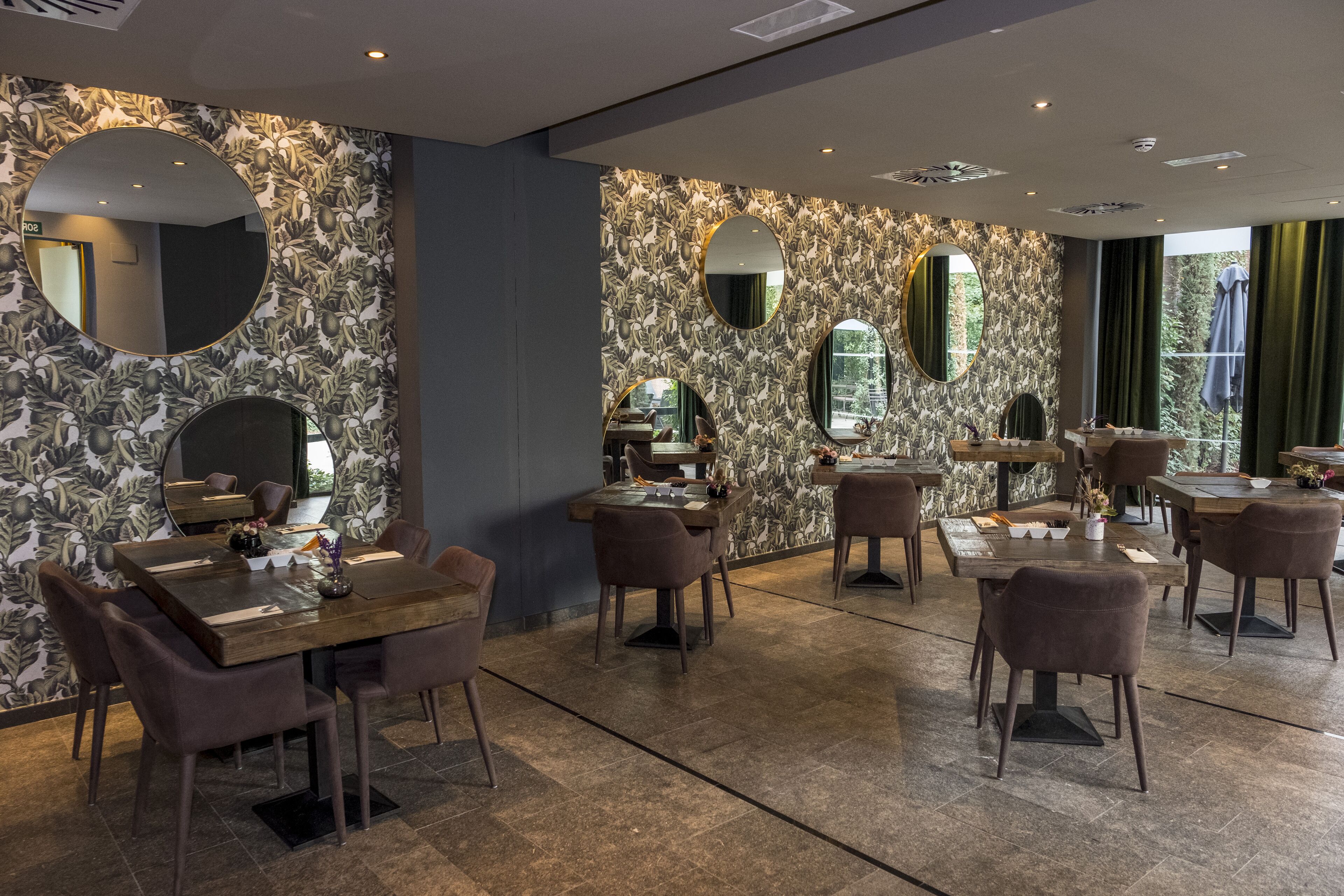 A restaurant with round tables and chairs, a patterned wall, and mirrors.