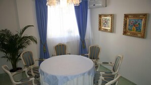 A dining area with a round table, six striped chairs, blue curtains, and two framed paintings on the wall. - Nelisse One Hotel Bucharest (Bucharest)