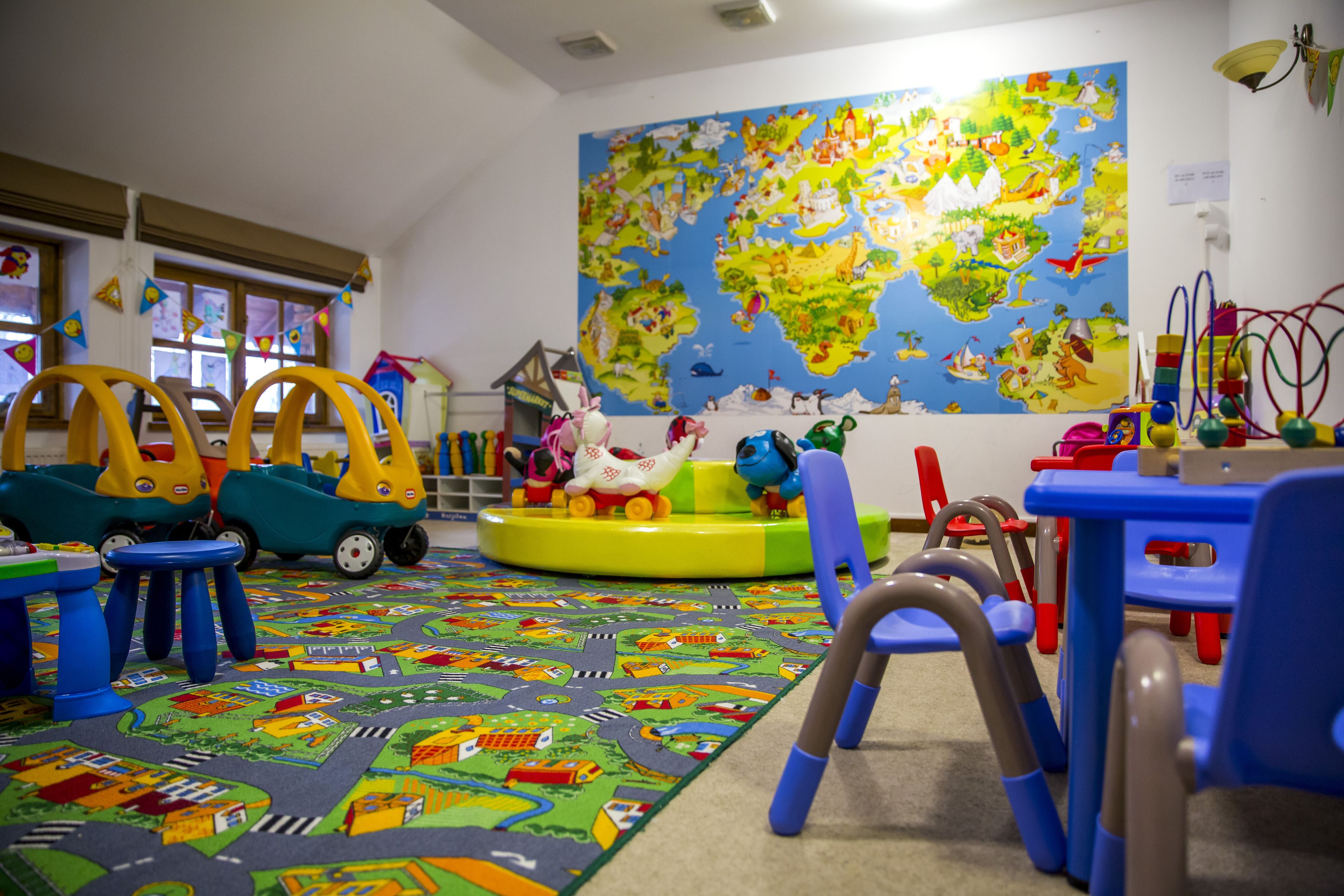 Une salle de jeux pour enfants avec des jouets colorés, une grande carte du monde accrochée au mur et un tapis aux motifs variés.