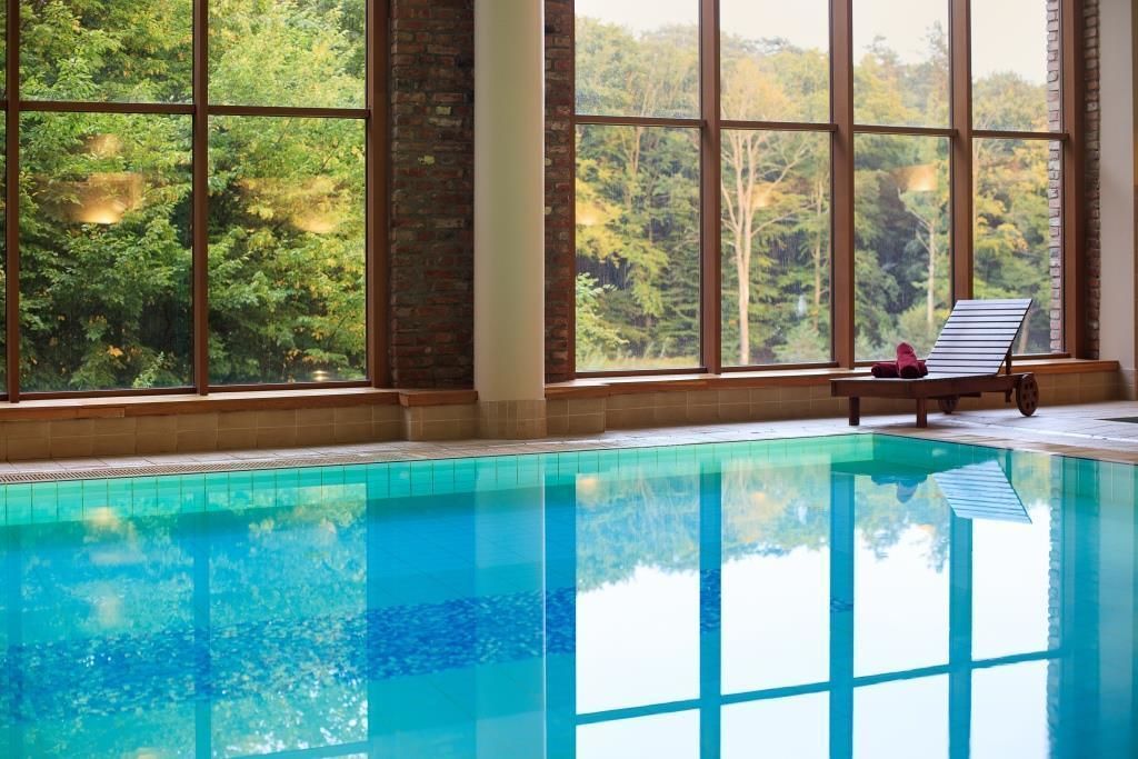 Ein Schwimmbad mit klarem, blauen Wasser, großen Fenstern und Blick auf eine bewaldete Gegend.