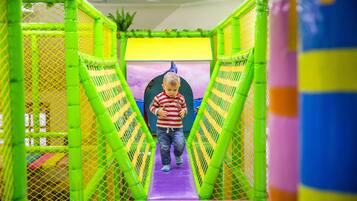 A child walking through a brightly colored indoor play area with netted walls and a slide.
