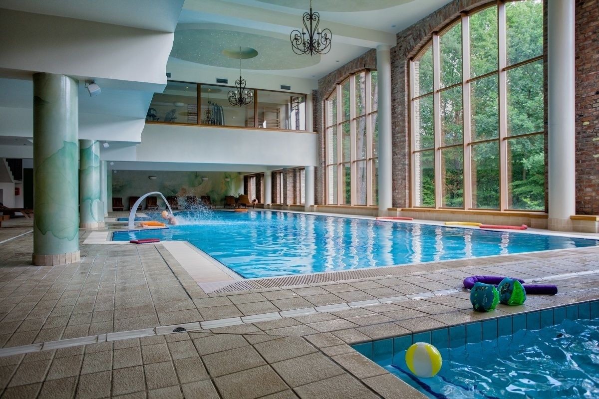 An indoor swimming pool with clear water, surrounded by large windows and a high ceiling.