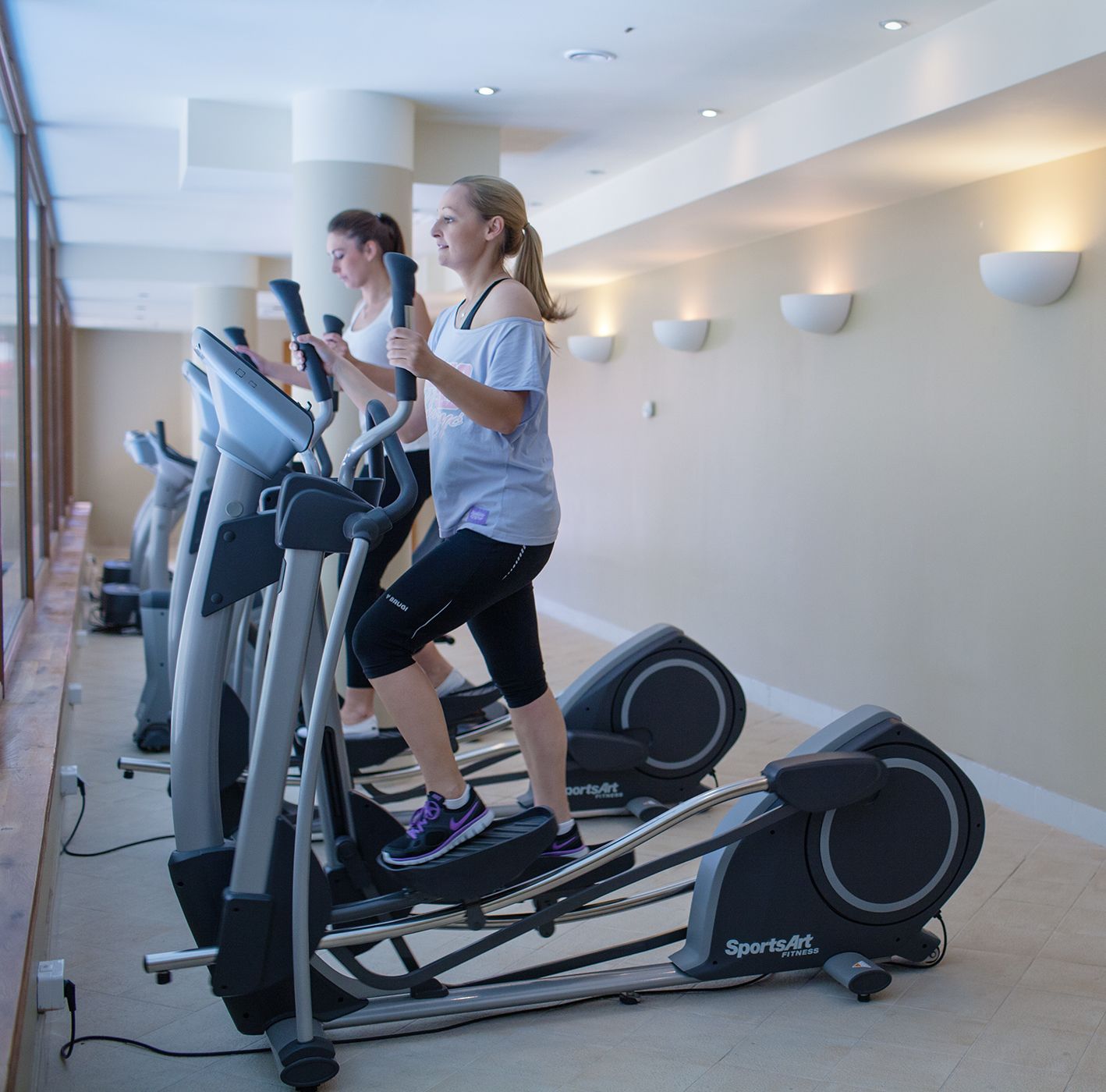 A gym with multiple treadmills, a modern interior, and wall-mounted lighting.