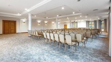 A large conference room with rows of chairs, a marble floor, and a projector screen.