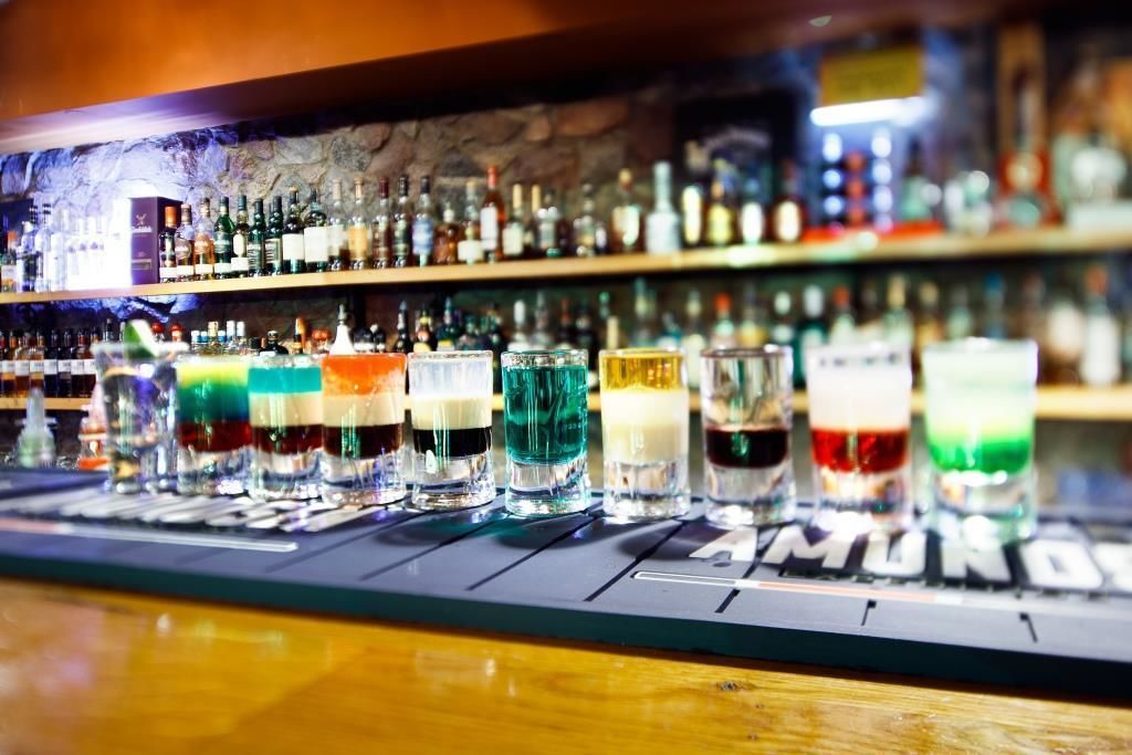 Un bar proposant une variété de boissons colorées et une sélection de bouteilles exposées sur des étagères à l’arrière-plan.