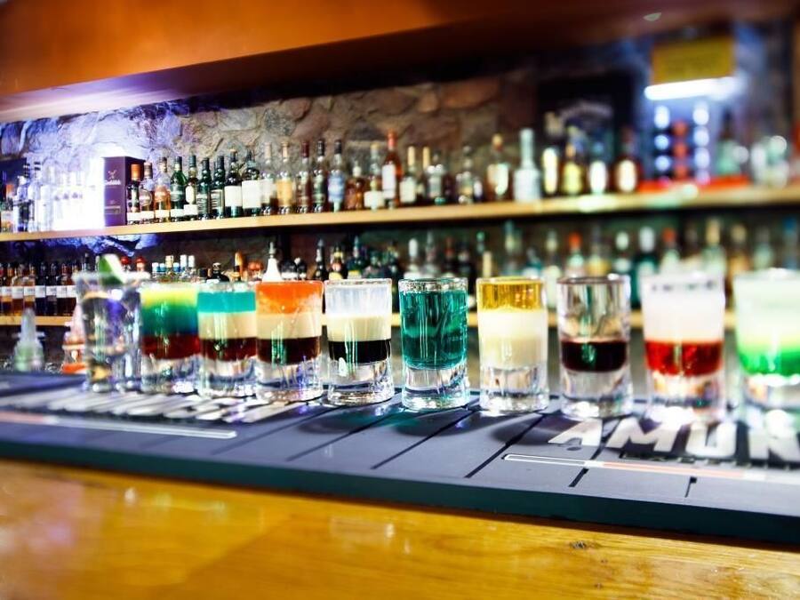 Un bar proposant une variété de boissons colorées et une sélection de bouteilles exposées sur des étagères à l’arrière-plan.