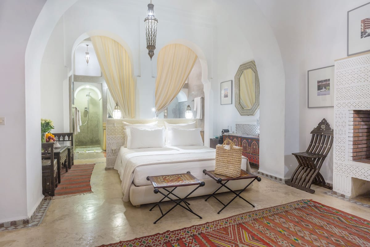 Um quarto espaçoso com uma cama grande, um espaço de estar com um banco, uma lareira e vista através de uma porta arqueada.