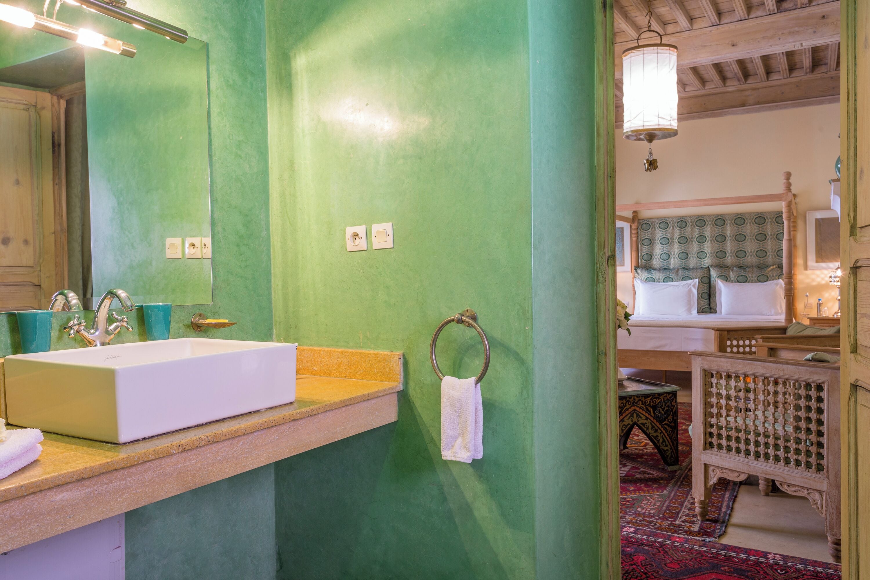 A bathroom with a green wall, a white sink, a mirror, and a wooden bench.