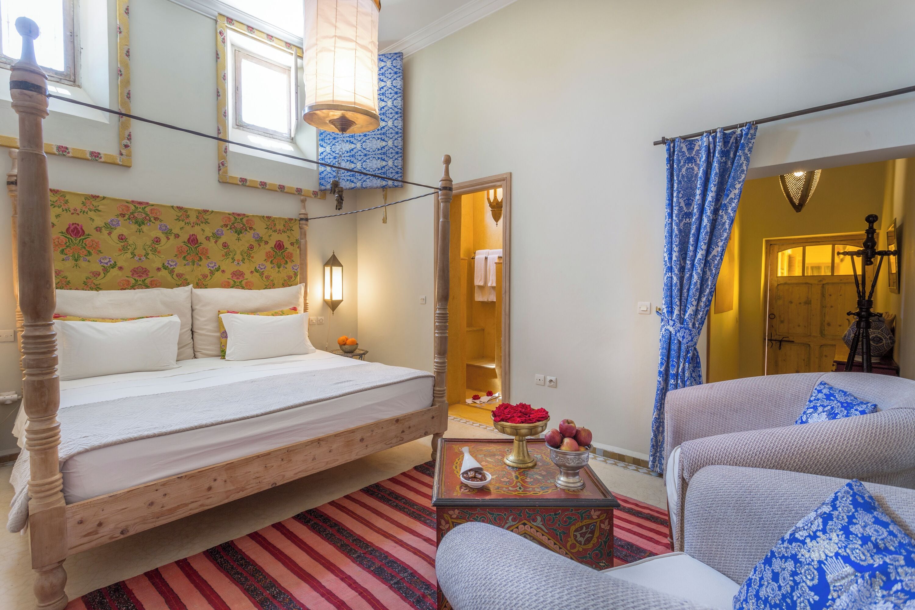Una habitación con una cama, una mesita con fruta, una silla y vistas al baño.