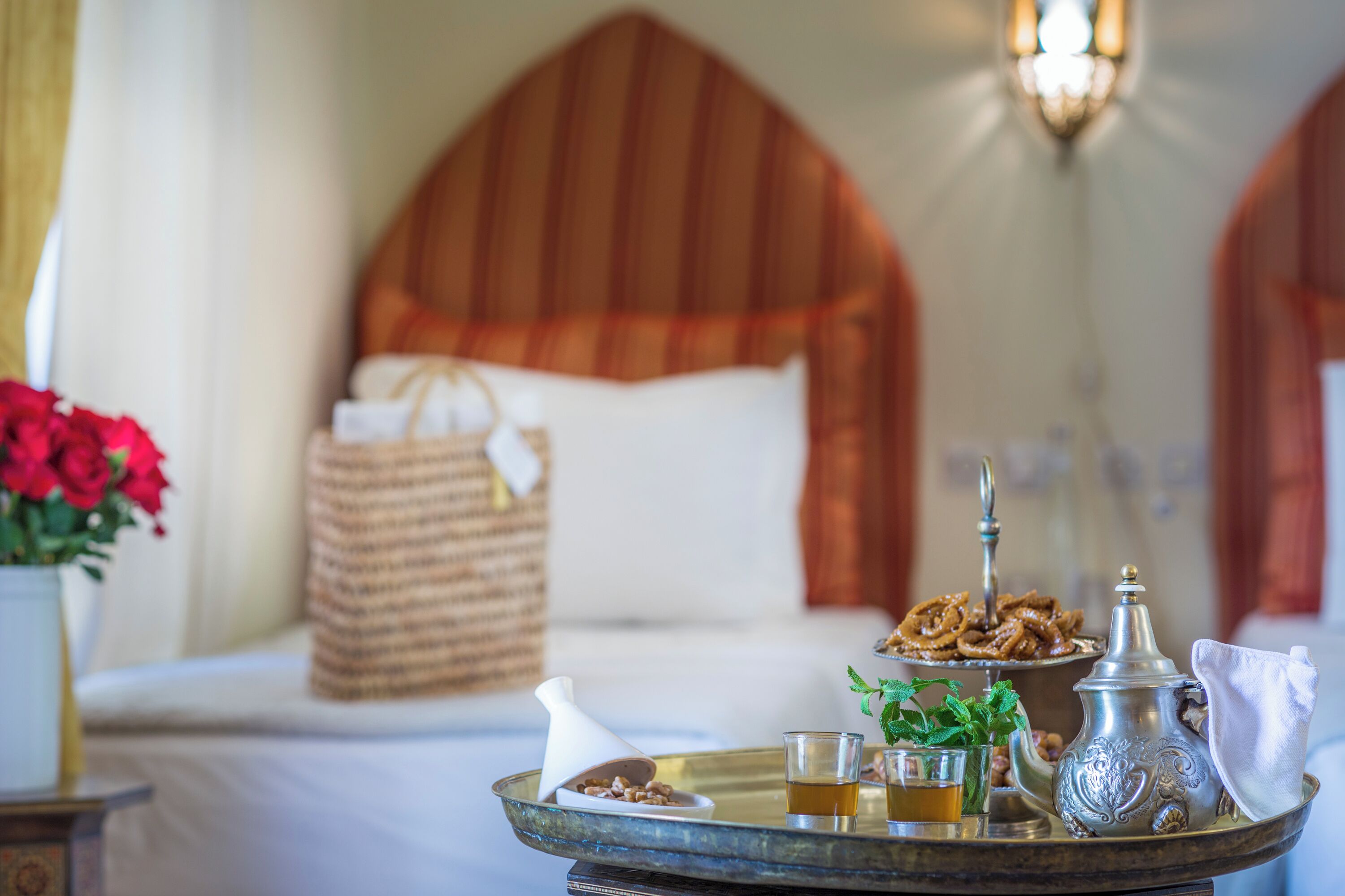 Un plateau de petit-déjeuner soigneusement préparé, avec une théière, des verres et une assiette de viennoiseries, posé sur un lit doté d’une tête de lit.