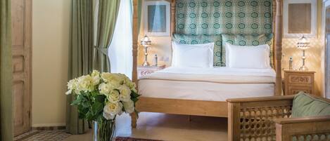 A four-poster bed with a patterned headboard, a bedside table with a lamp, and a vase of flowers on the floor.