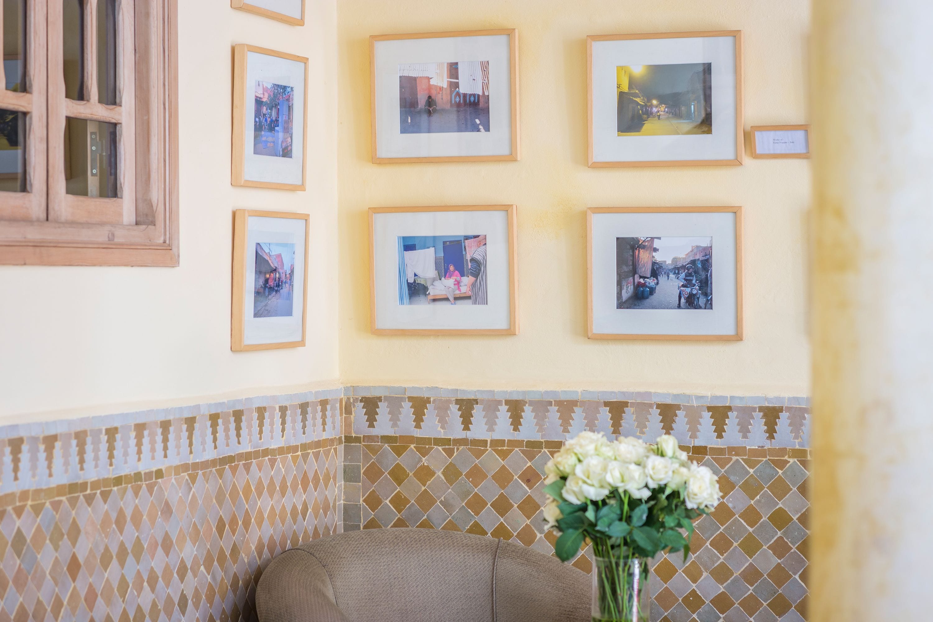 A corner of a room with a beige sofa, a wall with framed photographs, and a patterned tile border.